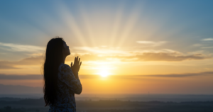 Pessoa orando por abundância ao nascer do sol com raios de luz divina